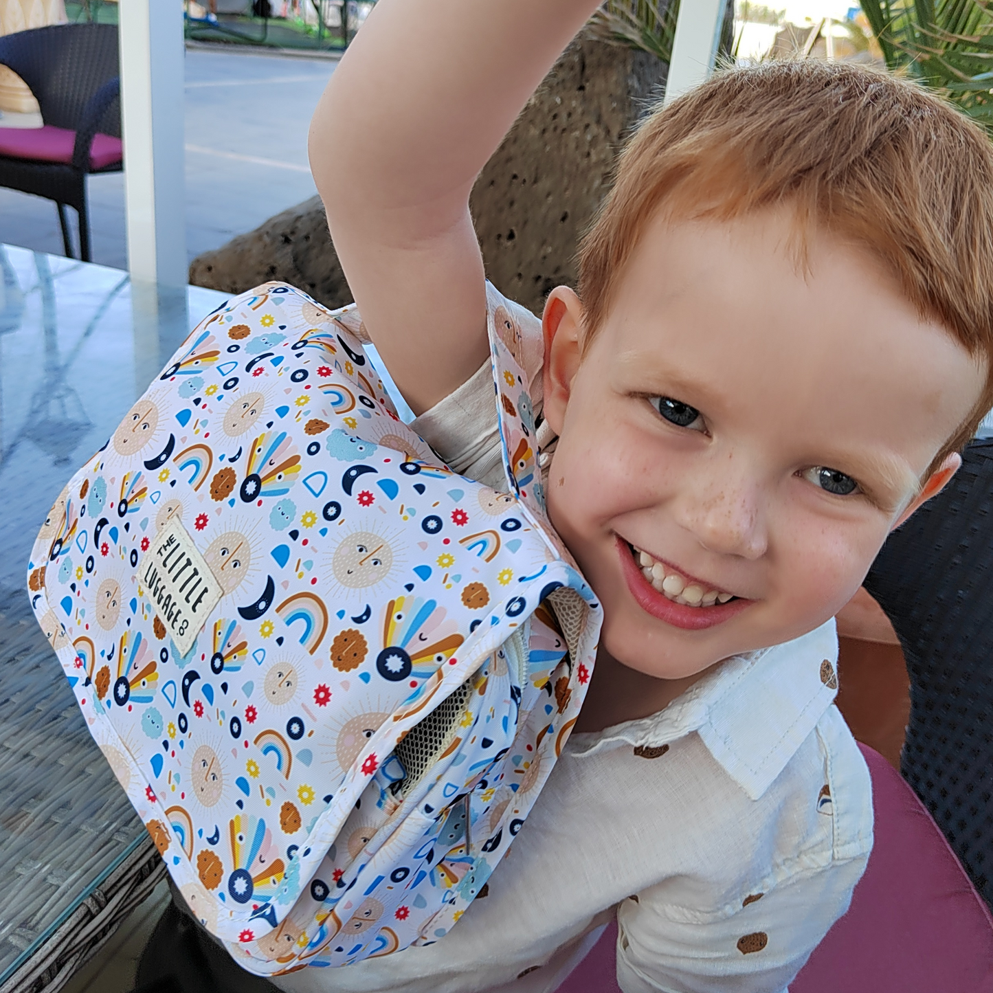 Child wearing a colorful backpack with a pattern of rainbows and shapes.