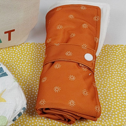 Orange fabric changing mat with sun pattern on a yellow and white polka dot background