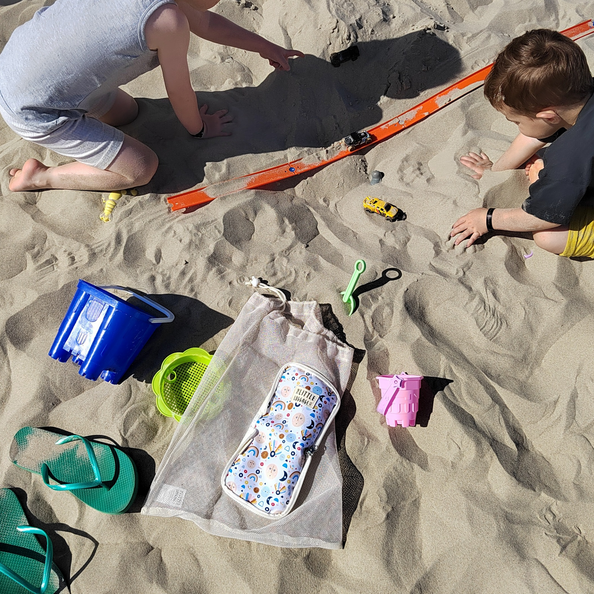 Children playing on a sandy beach with toys and a bag.