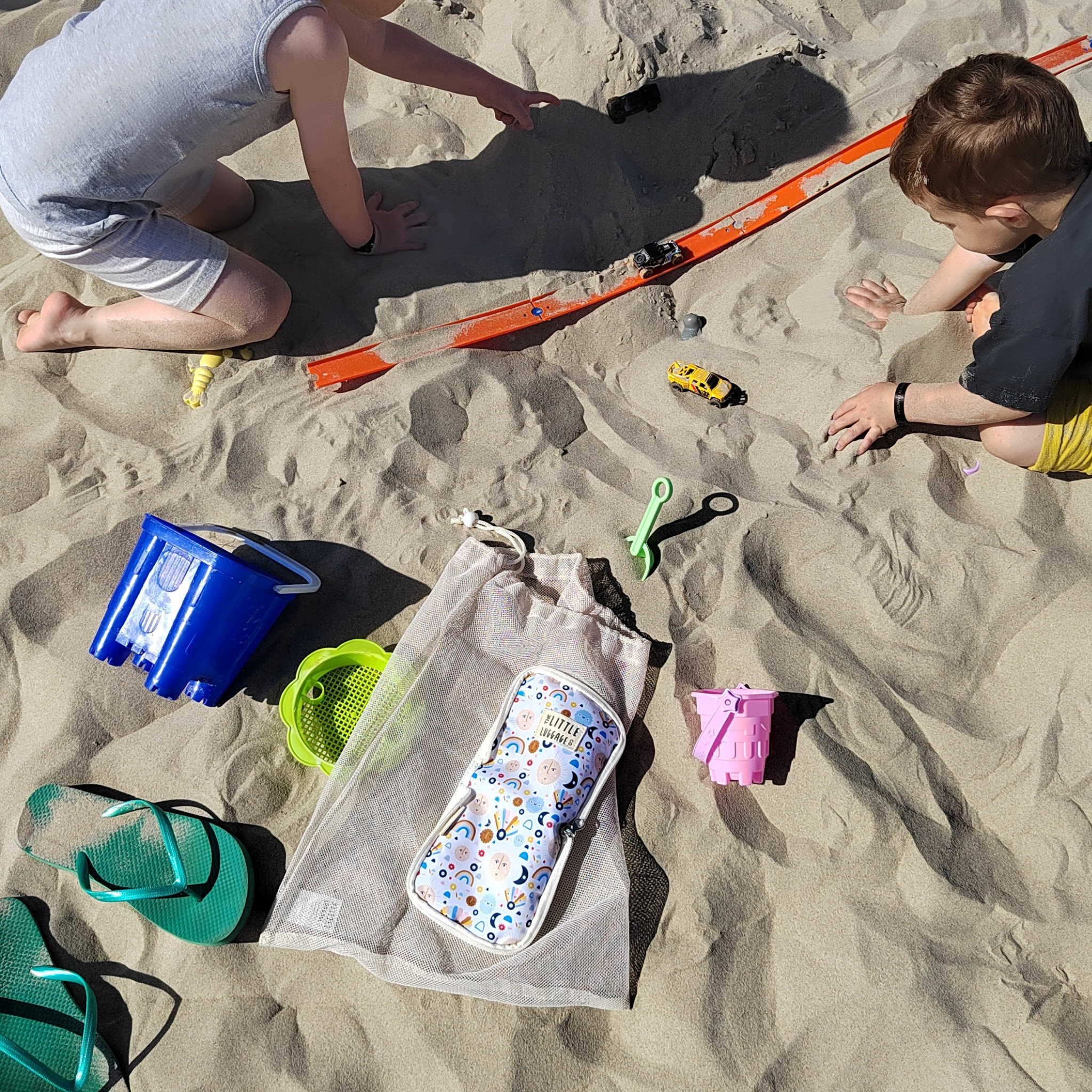 Children playing on a sandy beach with toys and a bag.